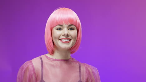 Portrait-Shot-Of-Charming-Woman-Wearing-A-Pink-Wig,-Posing-And-Smiling-To-Camera-On-Velvet-Background