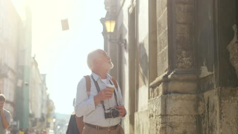 älterer-Tourist,-Der-Mit-Einer-Kamera-Und-Einem-Kaffee-In-Einer-Hand-Geht