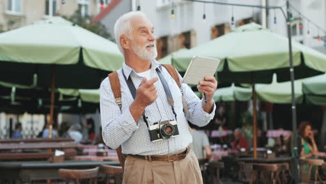 Senior-Tourist-With-Photocamera-Standing-Among-Tables-With-Umbrellas