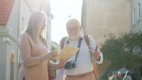 Couple-Of-Tourists-Standing-In-The-Sunlight-With-A-Map-In-Their-Hands-And-Looking-For-The-Route