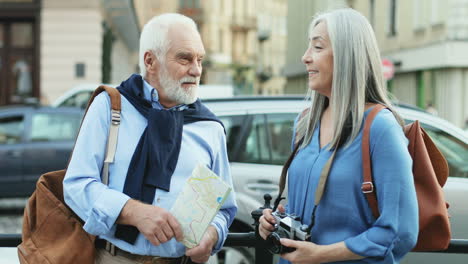 Portrait-Shot-Of-Senior-Couple-With-A-Map-Standing-In-The-Center-Of-The-City-And-Having-Conversation