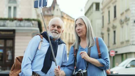 Glückliches-Seniorenpaar,-Das-Mit-Einem-Smartphone-Und-Einem-Selfie-Stick-Im-Freien-Steht