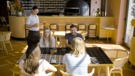 Group-Of-Friends-Sitting-At-A-Restaurant-Table-While-They-Talk-To-Each-Other