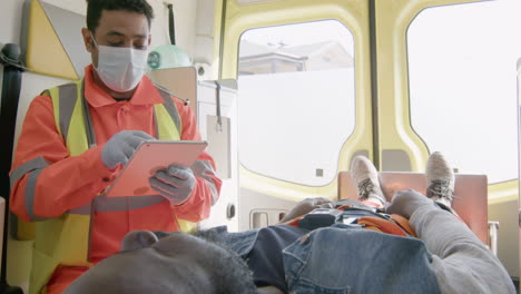 Paramédico-Masculino-Con-Máscara-Facial-Usando-Una-Tableta-Mientras-Viaja-En-Una-Ambulancia