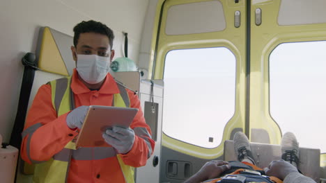 Paramédico-Masculino-Con-Máscara-Facial-Usando-Una-Tableta-Mientras-Viaja-En-Una-Ambulancia-1