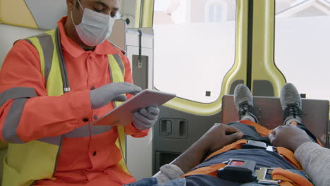 Paramédico-Masculino-Con-Máscara-Facial-Usando-Una-Tableta-Mientras-Viaja-En-Una-Ambulancia-2