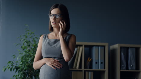 Schwangere-Frau-Mit-Brille-Telefoniert-Im-Büro-An-Ihrem-Arbeitsplatz