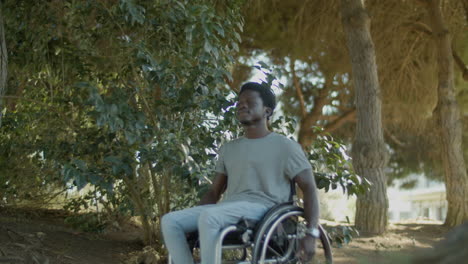 Black-Man-In-Wheelchair-Riding-Along-Park-Road-On-Summer-Day