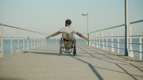 Back-View-Shot-Of-Black-Man-Riding-Wheelchair-At-Seafront