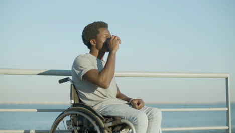 Junger-Mann-Im-Rollstuhl,-Der-Kaffee-Zum-Mitnehmen-Am-Meer-Genießt