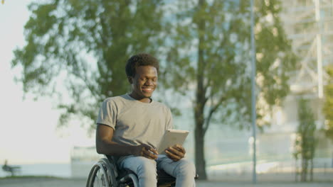 Young-Guy-In-Wheelchair-Having-Video-Chat-On-Tablet-In-Park