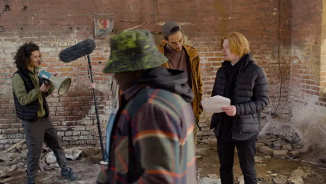 Two-Production-Coworkers-Talking-And-Reading-A-Document-About-The-Movie-In-A-Ruined-Building-The-They-Looks-At-The-Camera