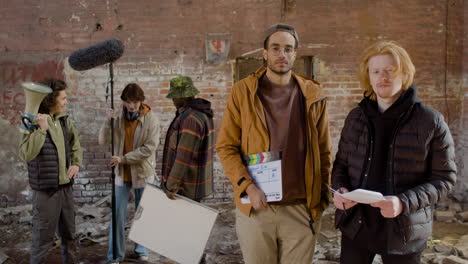 Two-Production-Coworkers-Looking-At-The-Camera-In-A-Ruined-Building-1