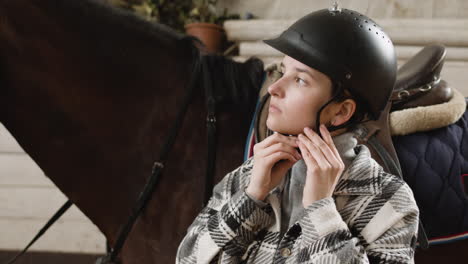 Young-Woman-Putting-A-Helmet-On-And-Petting-A-Brown-Horse