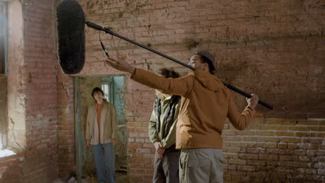 Man-Production-Worker-Holding-A-Microphone-On-A-Movie-Recording-In-A-Ruined-Building-1