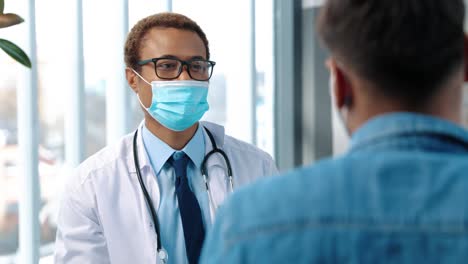 Close-Up-Of-Young-Handsome-Male-Doctor-Specialist-In-Medical-Mask-Talking-With-Young-Patient-Explaining-New-Coronavirus-Vaccine-On-Medical-Consultation,-Vaccination-Concept