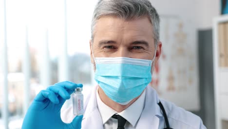 Close-Up-Of-Male-Healthcare-Specialist-Virologist-In-Protective-Uniform-And-Medical-Mask-Holding-In-Hand-In-Gloves-Ampoule-With-Coronavirus-Vaccine