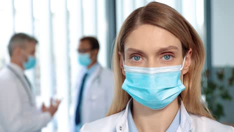 Portrait-View-Of-Young-Female-Assistant-Or-Doctor-Wearing-Medical-Gown-And-Protective-Mask-Standing-At-Medical-Ward-And-Looking-To-The-Camera
