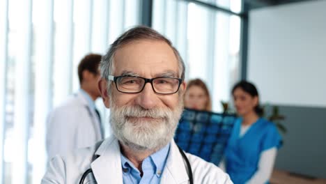 Portrait-Of-The-Senior-Confident-Doctor-Wearing-Medical-Gown-And-Glasses-Looking-At-The-Camera