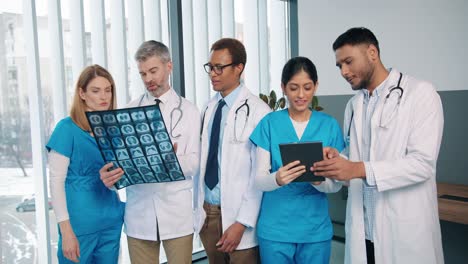Portrait-Of-Mixed-Races-Medical-Team-Standing-In-Hospital-Talking-Discussing-Coronavirus-Disease-Treatment,-Male-And-Female-Colleagues-Discuss-Patient-Analysis-And-Typing-On-Tablet,-Health-Concept