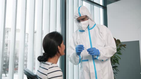 Portrait-Of-Healthcare-Specialist-Doctor-In-Protective-Suit-And-Gloves-Taking-From-Female-Patient-Sample-For-Pcr-Test-For-Coronavirus,-Working-In-Hospital-Laboratory,-Covid-Pandemic,-Analysis-Concept
