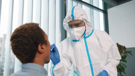 Nahaufnahme-Eines-Medizinischen-Laborspezialisten-In-Schutzuniform-Und-Medizinischer-Maske,-Der-Eine-Coronavirus-probe-Von-Einem-Männlichen-Patienten-Zum-Test-Nimmt-Und-Pcr-tests-Im-Klinikschrank-Durchführt