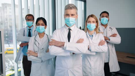 Portrait-Of-Serious-Experienced-Different-Mixed-Races-Healthcare-Workers-Doctors-And-Physicians-In-Medical-Masks-Posing-In-Clinic-Looking-At-Camera,-Quarantine-Concept,-Team-Colleagues