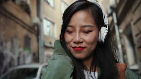 Close-Up-Of-The-Young-Charming-And-Happy-Stylish-Woman-In-Headphones-Going-The-Street-In-Slums-And-Listening-To-The-Music-Cheerfully