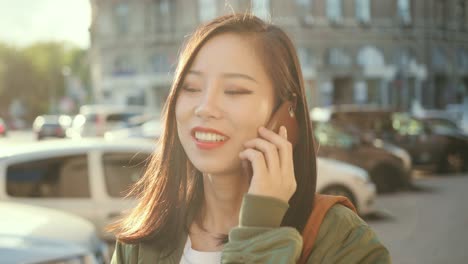 Close-Up-Of-The-Joyful-Young-And-Pretty-Girl-Talking-At-The-Phone-And-Laughing-At-The-Noisy-Street-Of-The-Town