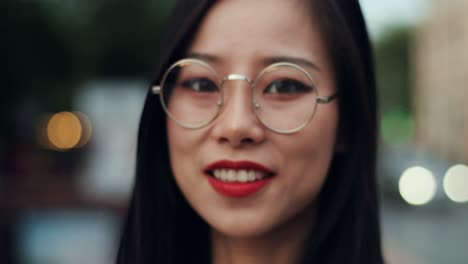 Portrait-Of-The-Young-Attractive-Woman-In-Glasses-Smiling-To-The-Camera-Cheerfully-Outdoors-At-The-Street,-First-Blurred-And-Then-In-Focus
