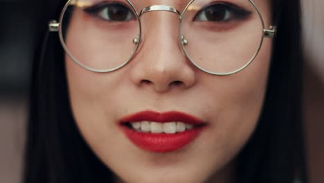 Close-Up-Of-The-Beautiful-Young-Girl-In-Glasses-Looking-Down-And-Then-Rising-Eyes-To-The-Camera-And-Smiling-Happily,-Blurred-And-Focused