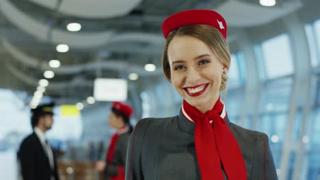 Porträt-Der-Charmanten-Jungen-Blonden-Stewardess-In-Uniform,-Die-Im-Flughafenterminal-Fröhlich-In-Die-Kamera-Schaut-Und-Lächelt