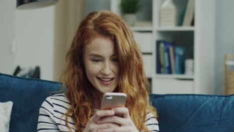 Close-Up-Of-The-Young-Beautiful-Red-Head-Girl-Sitting-On-The-Sofa-And-Typing-A-Message-Or-Scrolling-On-The-Smartphone-In-The-Living-Room