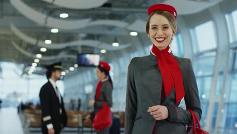 Porträtaufnahme-Der-Jungen,-Blonden,-Hübschen-Stewardess-In-Stylischer-Uniform,-Die-In-Der-Flughafenhalle-Steht-Und-Glücklich-Lächelt