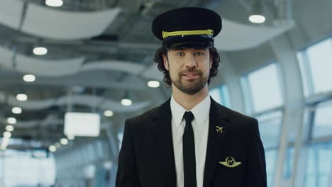 Close-Up-Of-Theyoung-Handsome-Man-Pilot-In-The-Uniform-And-His-Hat-Lokking-Straight-To-The-Camera-And-Smiling-In-The-Airport-Hall