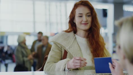 Pretty-Young-Girl-With-Long-Red-Hair-Coming-To-The-Checking-Desk-At-The-Airport-And-Giving-To-The-Female-Airport-Employee