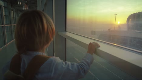 Nahaufnahme-Der-Rückseite-Des-Kleinen-Jungen,-Der-Am-Flughafenfenster-Steht-Und-Den-Wunderschönen-Sonnenuntergang-Betrachtet