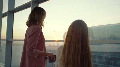 Back-View-On-The-Beautiful-Mother-And-Her-Teen-Little-Daughter-Standing-At-The-Airport-Window-And-Looking-Outside