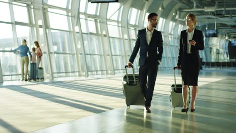 Business-Couple-Of-The-Co-Workers-Travelling-On-The-Working-Trip,-Walking-The-Airport-With-Suitcases-On-Wheels-And-Talking