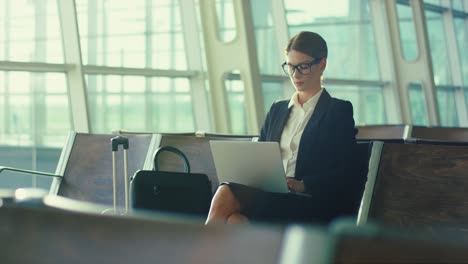 Portrait-Shot-Of-The-Attractive-Successful-Woman-In-Glasses-And-Business-Style-Sitting-With-The-Laptop-Computer-While-Waiting-For-Departure-In-The-Airport