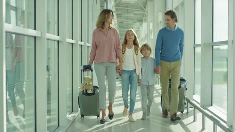 Nice-Cheerful-Mother,-Father,-Daughter-And-Son-Going-Through-The-Passage-In-The-Airport-With-Suitcases-On-The-Wheels-To-The-Plane-As-Having-Vacations-Tour