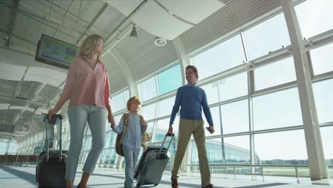 Parents-With-Small-Nice-Son-And-Big-Suitcases-On-Wheels-Passing-Through-The-Camera-In-The-Airport-Passage-While-Going-To-The-Departure-Or-Arrival-Gates