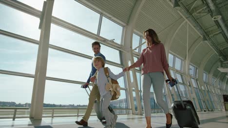 Parents-With-Small-Nice-Happy-Son-And-Big-Suitcases-On-Wheels-In-The-Airport-Passage-While-Going-To-The-Departure-Or-Arrival-Gates