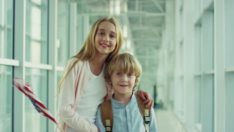 Portrait-Shot-Of-The-Happy-Kids,-Girl-And-Boy,-Standing-In-The-Airport-And-Smiling-To-The-Camera-With-American-Flag-1