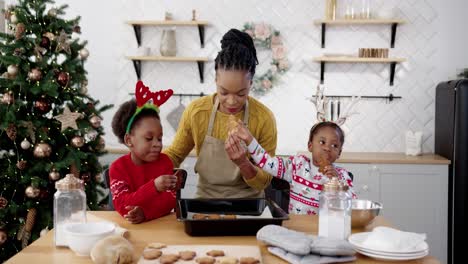 Mom-With-Little-Pretty-Kids-Standing-At-Table-In-Home-Kitchen-Ornate-Xmas-Cookies-Add-Colorful-Sprinkles-Decorate-Biscuits
