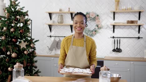 Happy-Woman-In-Apron-Standing-At-Table-In-Home-Cozy-Kitchen-And-Holding-Tray-With-Xmas-Cookies-Add-Decorated-Biscuits