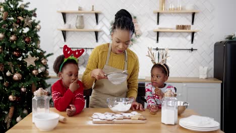 Happy-Family-With-Little-Cute-Kids-On-Christmas-Standing-At-Table-In-Kitchen-And-Decorate-Homemade-Baked-Xmas-Gingerbread-Cookies-New-Year-Preparations,-Winter-Season-Holidays-Concept