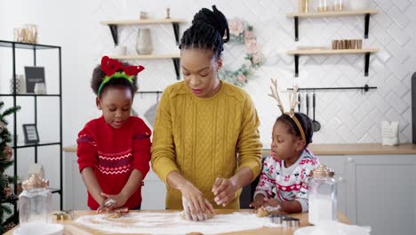 Happy-Mother-With-Little-Cute-Kids-Standing-At-Table-In-Home-Christmassy-Decorated-Kitchen-And-Making-Dough-For-Xmas-Cookies