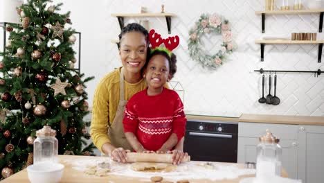 Portrait-Of-Happy-Mom-With-Little-Cute-Kid-In-Xmas-Sweater-Standing-At-Table-In-Home-Decorated-Kitchen-And-Smiling-To-Camera-While-Making-Dough-For-Christmas-Gingerbread-Cookies