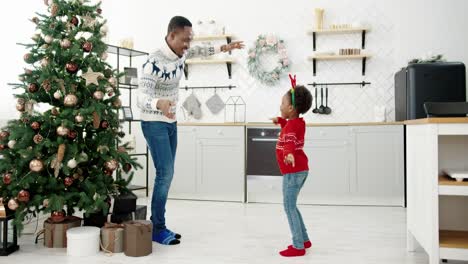 Dad-And-Little-Child-Listen-To-Xmas-Music-And-Dancing-In-Modern-Home-Kitchen-Decorated-With-New-Year-Tree-On-Christmas-Eve-Happy-Family-Enjoy-Free-Time-And-Having-Fun-Holidays-Concept